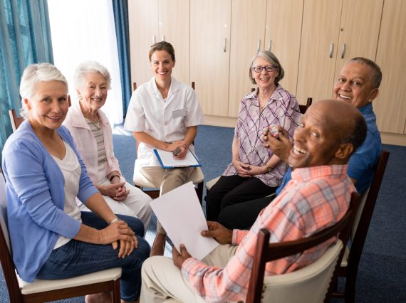 High angle portrait of smiling seniors and female doctor sitting on chairs at retirement home